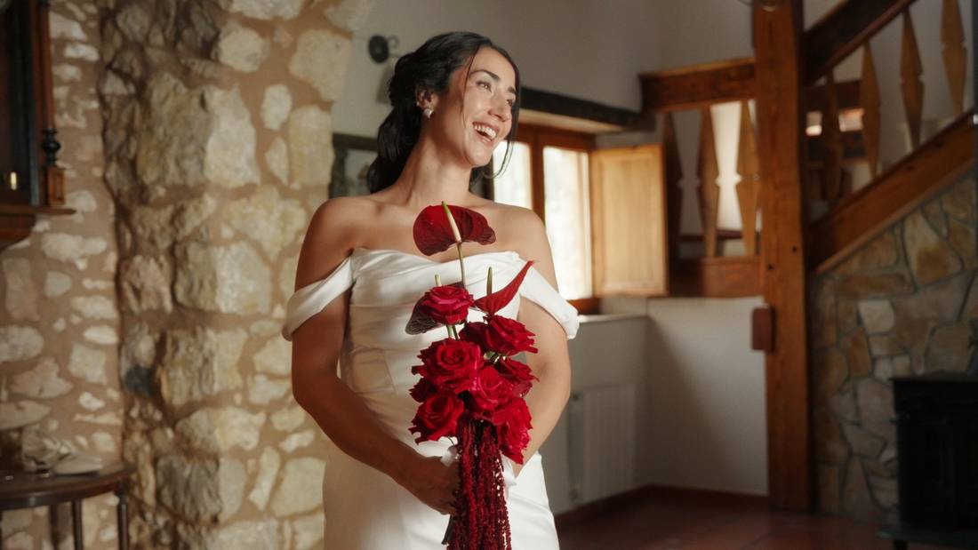 La novia sonríe con un ramo de rosas rojas